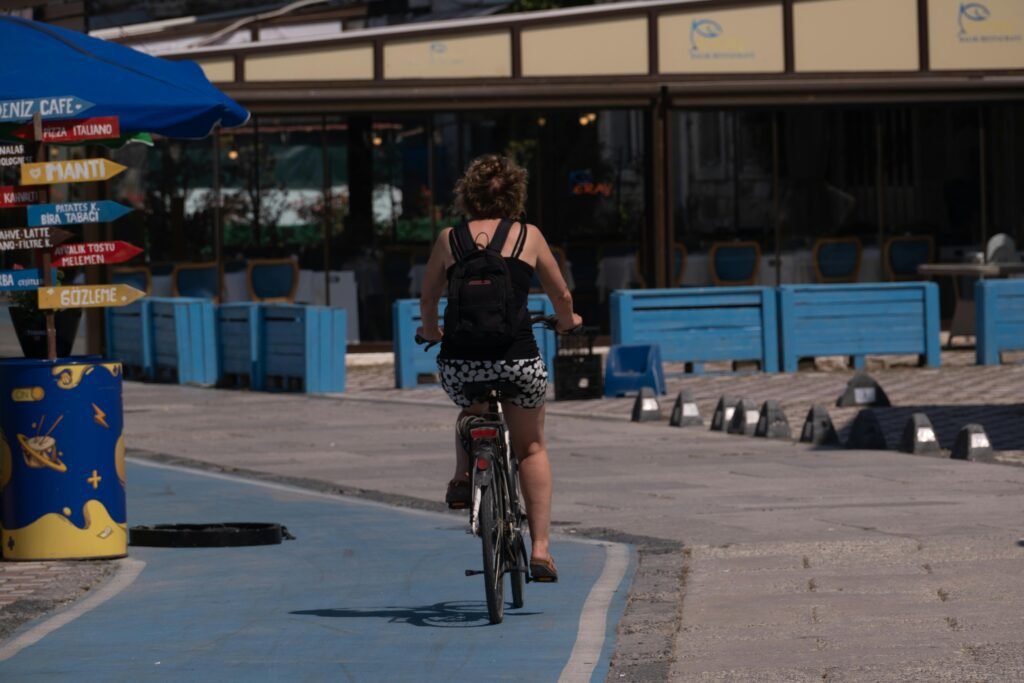 Rear view of a woman cycling on a coastal path in Foça, İzmir, Türkiye on a sunny day.