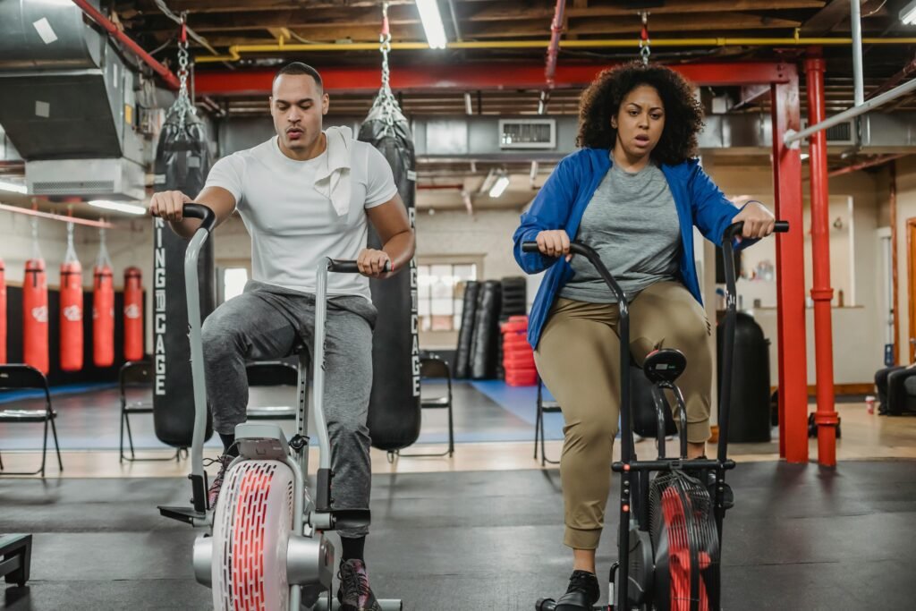 Full body of focused curvy female and muscular male instructor training on exercise bikes in spacious gym